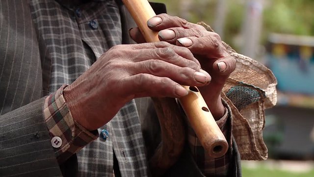  busker in a village in Peru. Close up to the hands playing a flute.