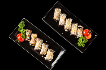 Eggplant rolls with cheese, garlic and sesame on black plates with herbs and tomato. Top view and isolated on black