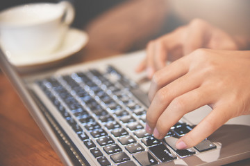 Close up Woman hands typing on laptop with cup of coffee on wooden table.