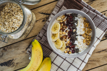 Oatmeal with bananas, cranberry, chia seeds, coconut shreds, almonds. Healthy breakfast concept. Rustic wooden background.