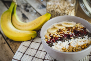 Oatmeal with bananas, cranberry, chia seeds, coconut shreds, almonds. Healthy breakfast concept. Rustic wooden background.