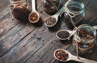 Different kinds of tea in jar and wooden spoons on wood table