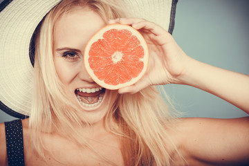 Woman holding red grapefruit fruit wearin sun hat