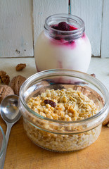 Healthy breakfast of oatmeal with nuts and berry yogurt in a glass bowl on a wooden board and old white shabby wooden background
