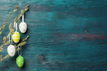 Easter eggs hanging on willow branches over rustic wooden background © Vitaliy