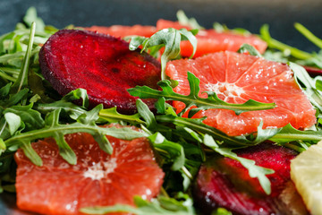 Fresh mix salad of red beet, grapefruit and orange on a cushion of arugula in a black dish. Closeup view.