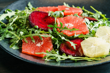 Fresh mix salad of red beet, grapefruit and orange on a cushion of arugula in a black dish. Closeup view.