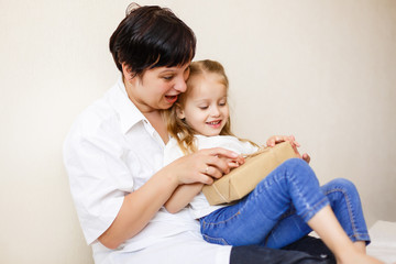 Beautiful brunette woman showing a book to her baby while sitting on a bed in her apartment