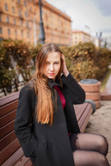portrait Beautiful young brunette woman sits on a bench in the city..