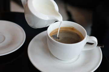 Pouring cream into a cup of coffee