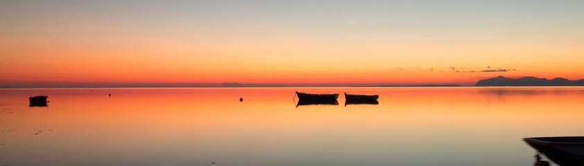 A warm sunset on a calm water, with Islands in the background