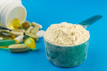 Protein powder in measuring plastic spoon and vitamin complex, omega 3, glucosamine capsules,...