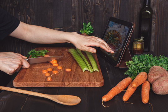 Woman following recipe on tablet and cooking healthy meal in the kitchen, cutting vegetables on the wooden table