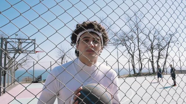 Portrait of a basketball player standing with ball near gread on basketball court, slow motion. dolly shot