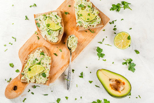 Homemade sandwich toasts with with guacamole, lime lemon and parsley on white table, copy space top view