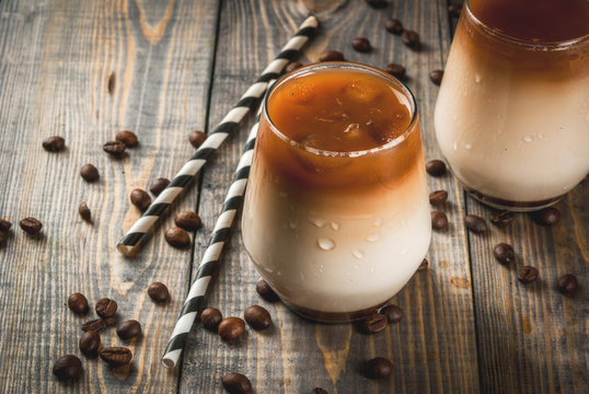 Cold coffee with milk, caramel and ice, with cubes of frozen coffee. Cappuccino, frapuchchino or latte. On awooden dark table, with coffee beans and striped straws. Copy space