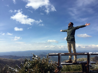 Happy young man celebrates freedom at the top of the mountain