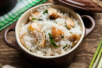 Tasty rice with chicken in saucepan on wooden table
