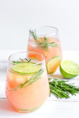 glass of fresh juice with lime and rosemary on white table background
