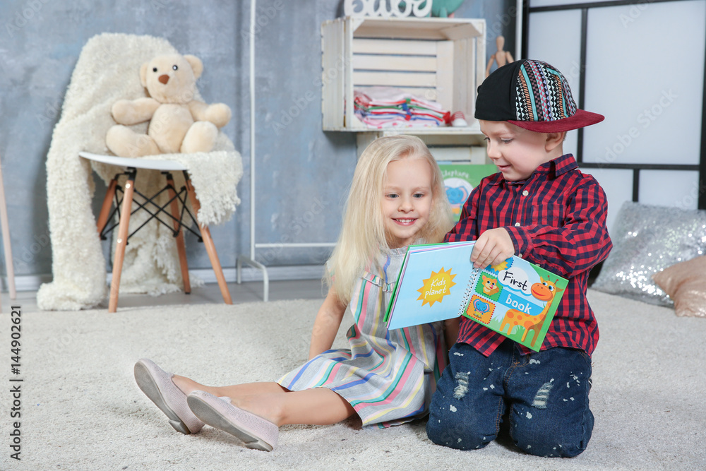 Wall mural Cute funny children sitting on carpet with book