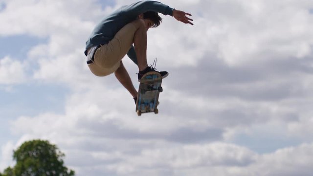 Camera tilts up as a skateboarder does a high aerial jump, in slow motion