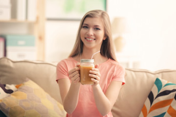 Young woman tasting fresh juice sitting on couch at living room