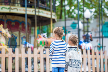 Adorable little girls near the carousel outdoors