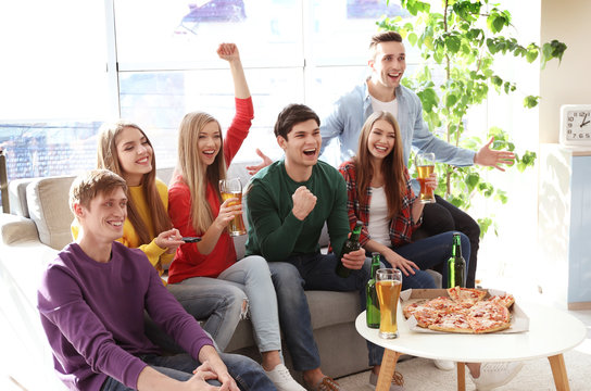 Friends with tasty pizza and beer watching sports on TV at home