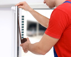 Young worker applying rubber strip onto window in office