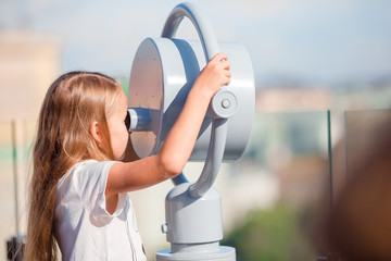 Little girl looking at coin operated binocular on terrace with beautiful view
