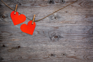 Two red paper hearts Valentines hanging on the rope on the clothespin. Wooden background texture