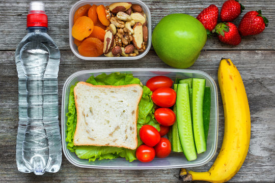 Healthy lunch boxes with sandwich and fresh vegetables, bottle of water, nuts and fruits