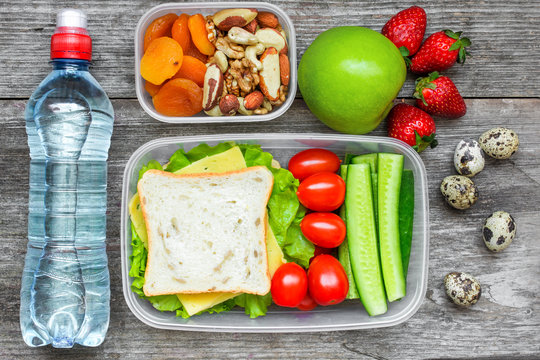 Healthy lunch boxes with sandwich, eggs and fresh vegetables, bottle of water, nuts and fruits