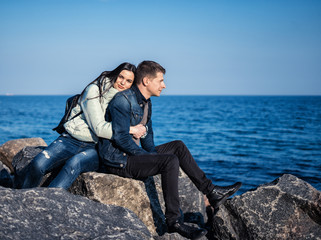emotional couple sitting on the rocks on the beach with ocean on background. She is hugging him from behind.