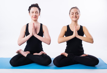 Two women doing yoga and meditating in lotus position isolated on white background.