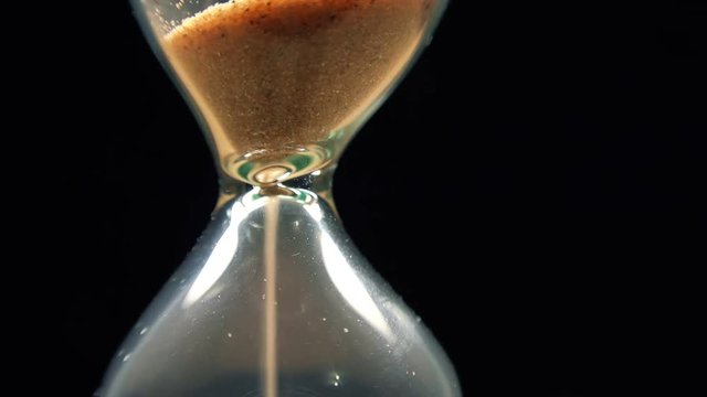 Close-up View of Sand Flowing Through an Hourglass on black background. 4K
