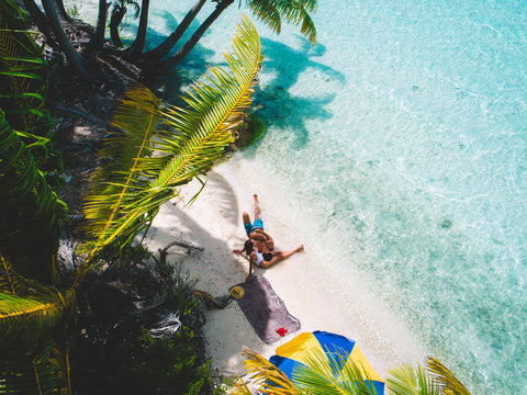Aerial view of couple relaxing on island beach with palm trees, Tahiti, South Pacific