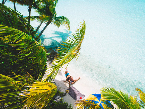 Aerial view of couple relaxing on island beach with palm trees, Tahiti, South Pacific