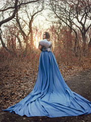A big, beautiful woman in a blue raincoat with a long train, walks in the mountains. Creative colors