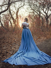 Naklejka premium A big, beautiful woman in a blue raincoat with a long train, walks in the mountains. Creative colors