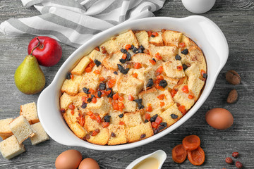 Freshly baked bread pudding in casserole dish and ingredients on wooden table