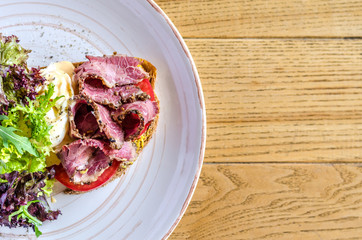 A sandwich with ham cheese and herbs on a white plate, on a wooden table. View from above