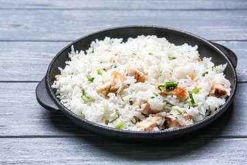 Frying pan with delicious rice and chicken on wooden table