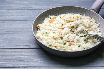 Frying pan with delicious rice and chicken on wooden table