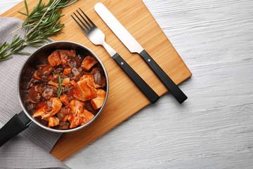 Saucepan with chicken cacciatore on wooden board