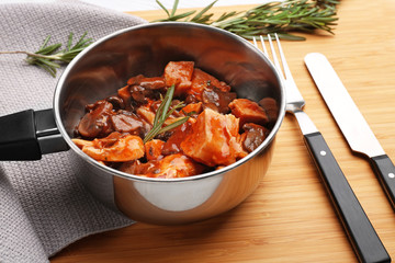 Saucepan with chicken cacciatore on wooden board