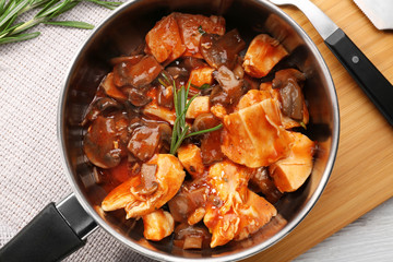Saucepan with chicken cacciatore on wooden board
