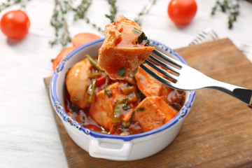 Fork with piece of meat over chicken cacciatore in bowl, closeup
