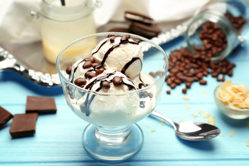 Tasty ice cream with candies and chocolate topping in bowl on wooden table