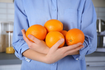Woman holding armful of oranges in kitchen